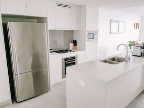 Eine moderne Küche mit einem Edelstahl-Kühlschrank, einem eingebauten Ofen und einer großen Kochinsel mit Spüle.
