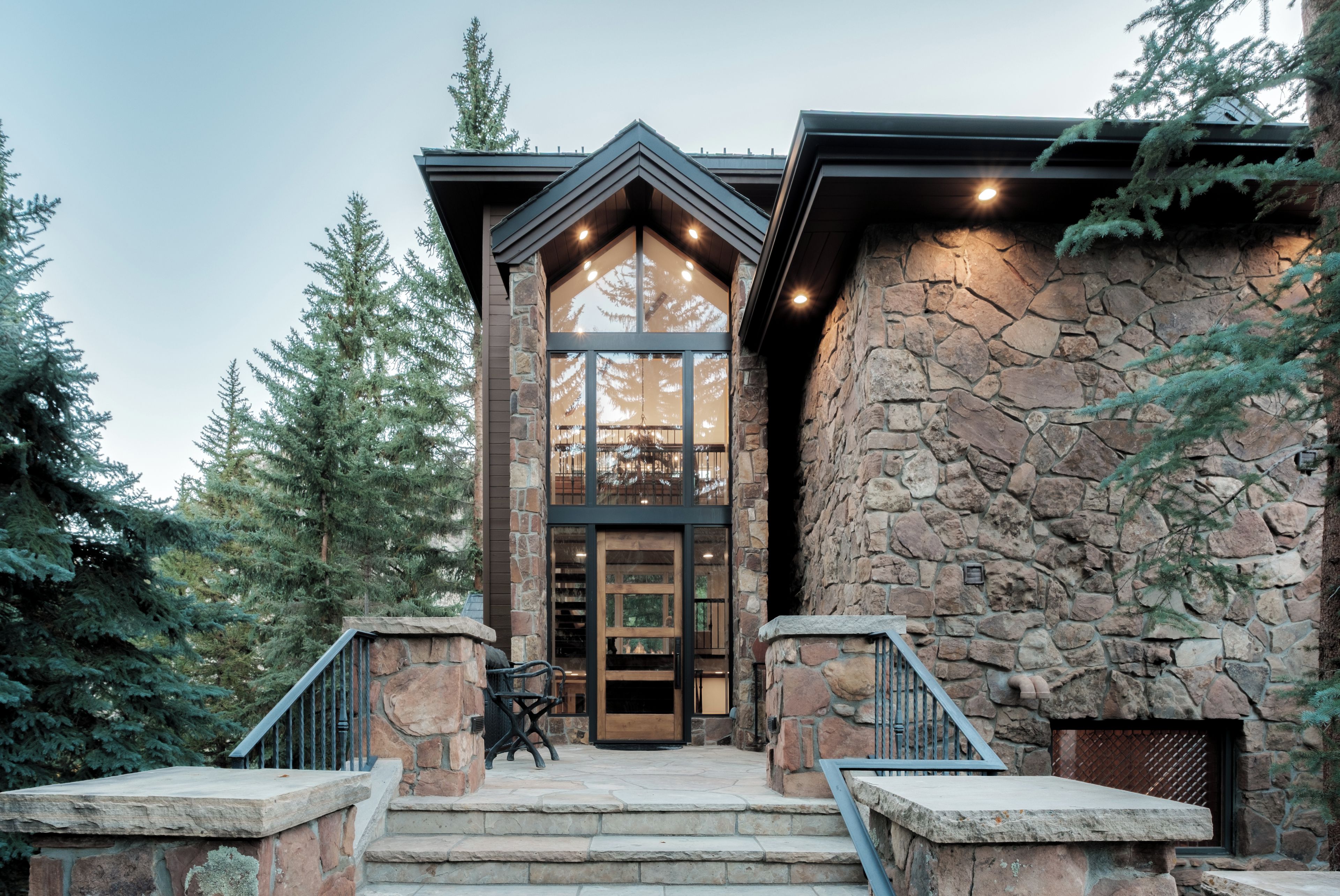 A stone building with a large glass entrance, wooden steps, and a metal railing.