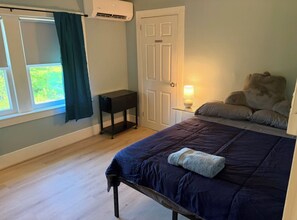 A bedroom with a bed, a bedside table with a lamp, a door, and a window with curtains. - Historical 5-bed brick home with modern amenities (Hinsdale)