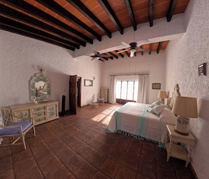 Une chambre spacieuse avec un grand lit, deux ventilateurs de plafond, une commode et une chaise.