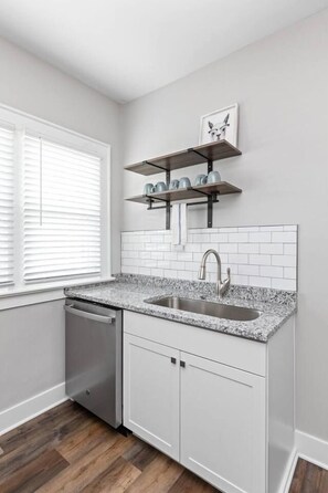A kitchen with white cabinets, a granite countertop, a stainless steel sink, and a window with blinds. - Earthy Escape - 5 min to downtown (Indianapolis)