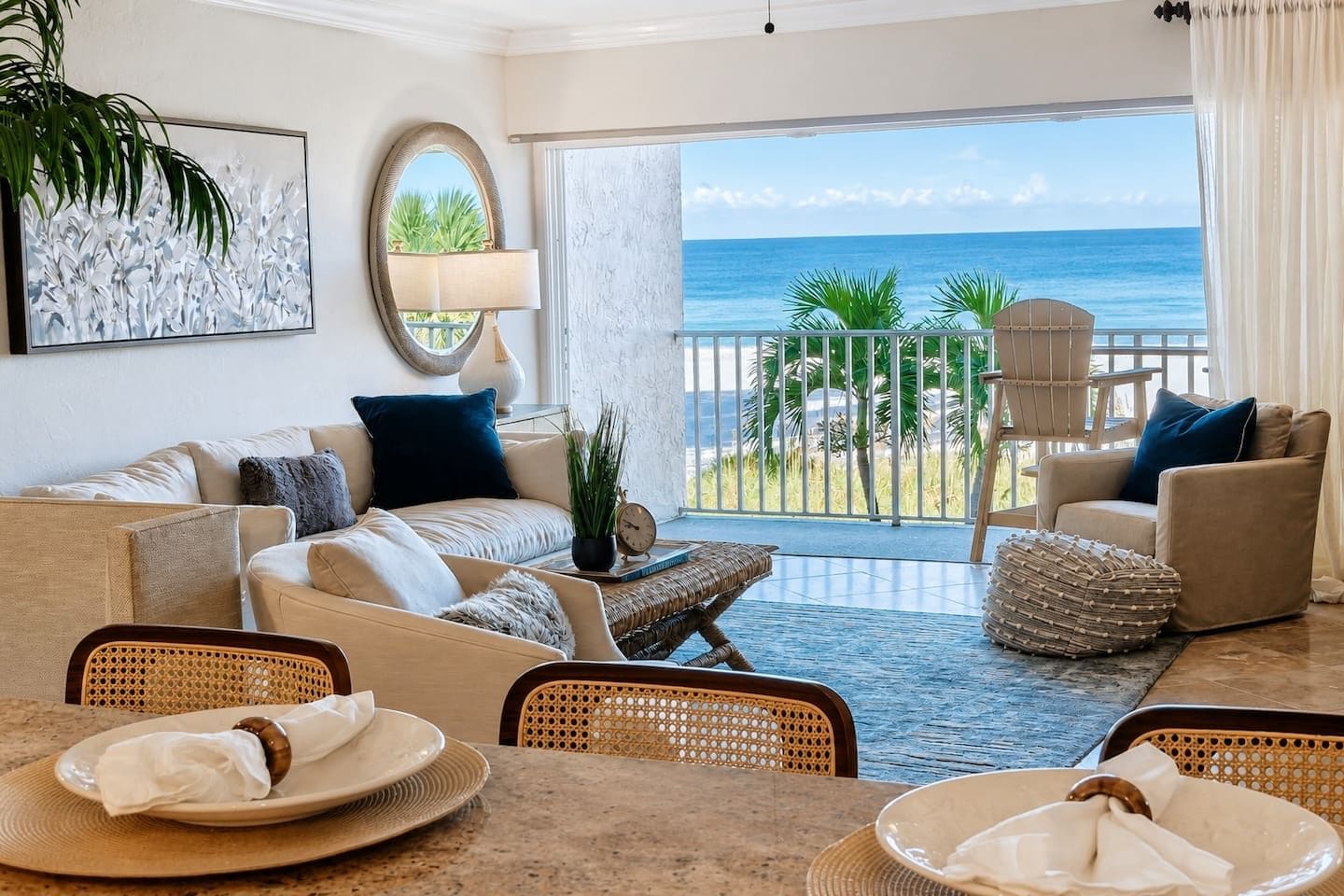 A hotel room with a balcony, a sofa set, a dining table with plates, and a view of the ocean.