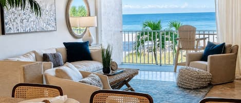 A hotel room with a balcony, a sofa set, a dining table with plates, and a view of the ocean.