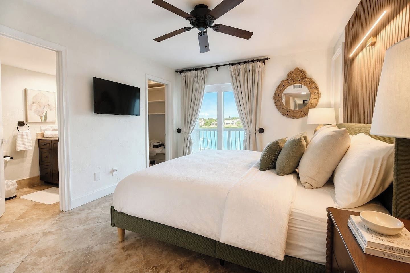 Un dormitorio con cama, ventilador de techo, televisión y vistas al exterior.