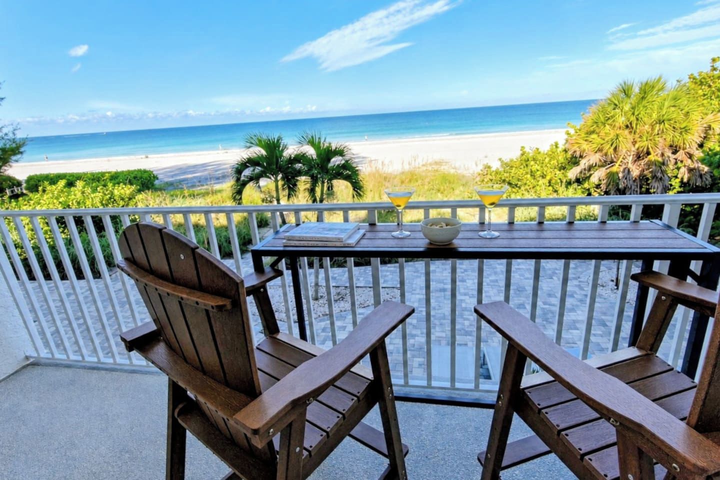 Mesa de madera con dos sillas en un balcón con vista a la playa.