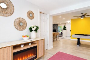 A modern living room with a fireplace, a dining area, a yellow accent wall, and a pool table. - Clearwater Fun House, Games, Heated Pool, Hot Tub Sleeps12 (Clearwater)