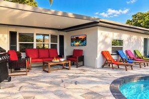A modern outdoor living area with a pool, red outdoor furniture, and colorful lounge chairs. - Clearwater Fun House, Games, Heated Pool, Hot Tub Sleeps12 (Clearwater)
