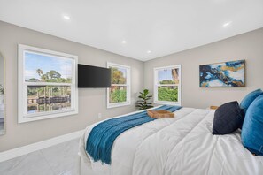 Une chambre à coucher comprenant un lit, un téléviseur à écran plat et trois fenêtres équipées de stores.
