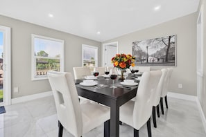 A dining room with a dark wooden table, white chairs, and a vase of flowers. - Spacious Waterfront Home | 4BR | Near Downtown (Tampa)