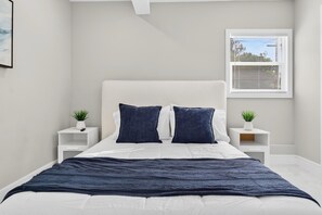 A bedroom with a bed, two bedside tables, a window with blinds, and a small plant on each table. - Spacious Waterfront Home | 4BR | Near Downtown (Tampa)