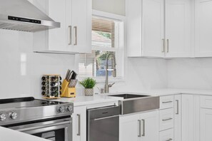 Une cuisine moderne avec des meubles blancs, des appareils en acier inoxydable et une fenêtre équipée de stores.