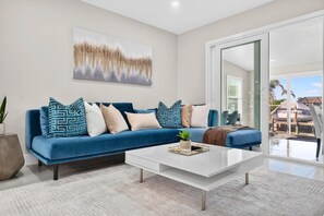 A modern living room with a blue sofa, white coffee table, and a large window offering a view of the outdoors. - Spacious Waterfront Home | 4BR | Near Downtown (Tampa)