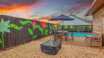 Un jardin avec une piscine, une table de patio couverte et une clôture ornée de peintures murales représentant des fleurs aux couleurs vives.