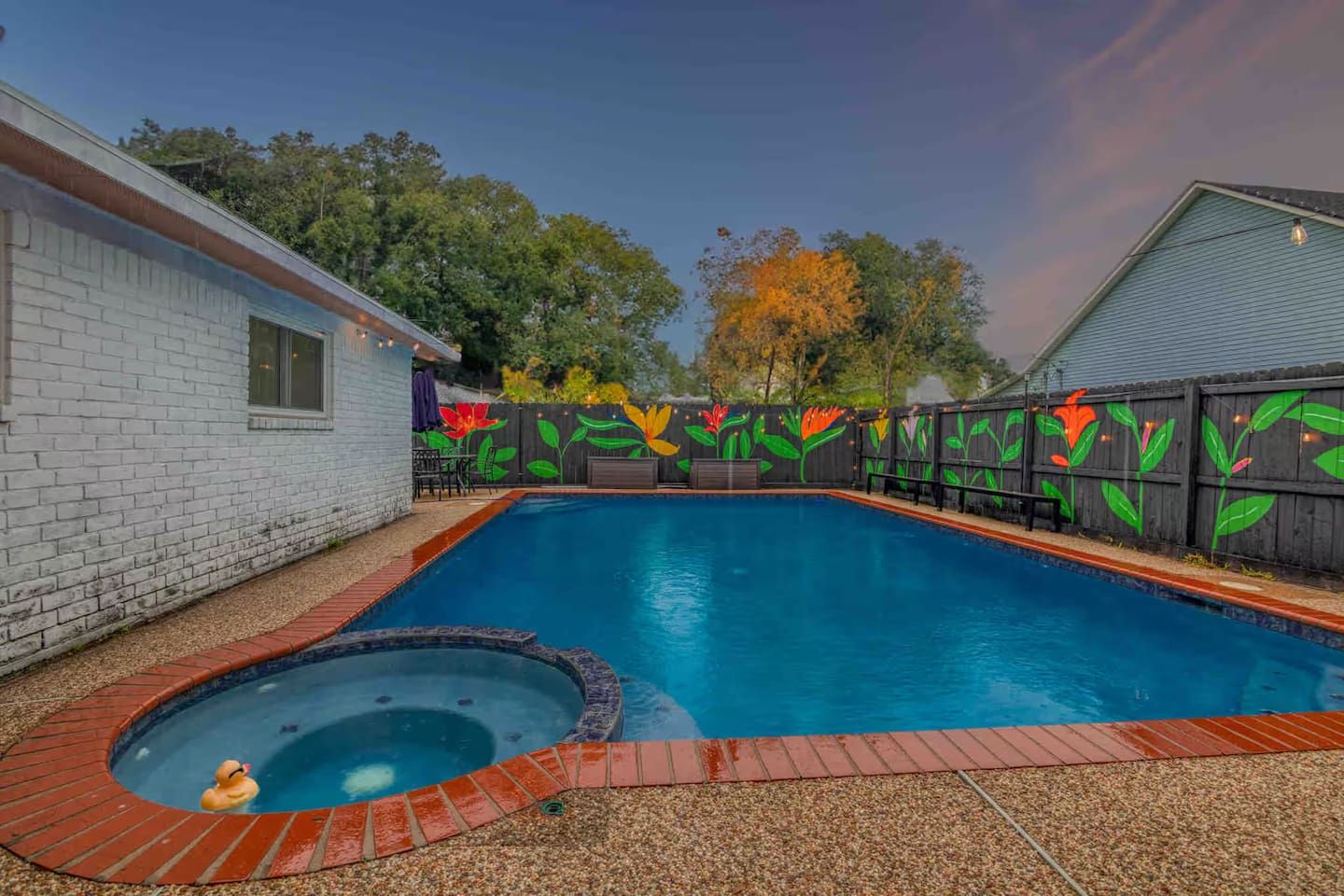 A swimming pool with a hot tub, surrounded by a brick deck and a wooden fence with colorful floral murals.