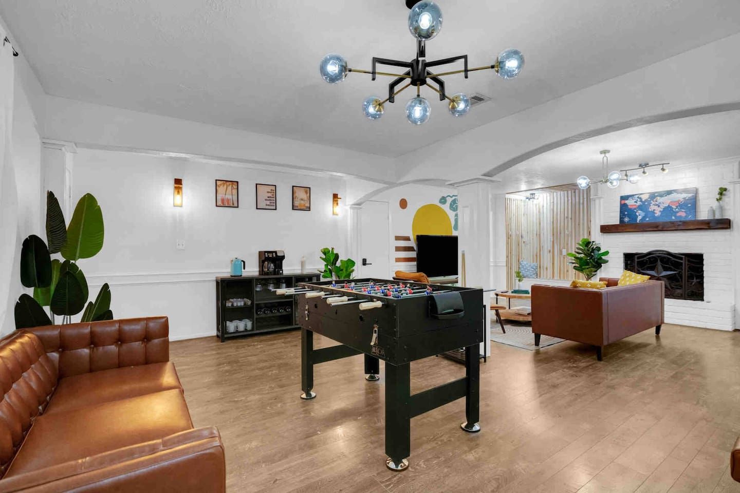 A spacious living room with a foosball table, a brown leather sofa, a coffee station, and a fireplace.