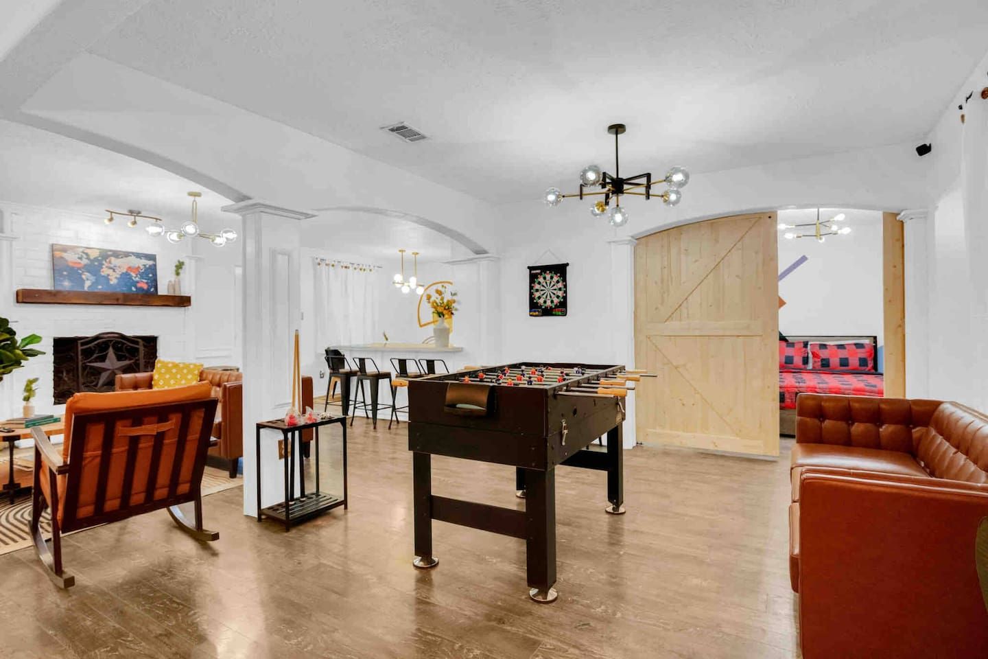 A spacious living room with a foosball table, leather sofas, a dining area, and a dartboard.