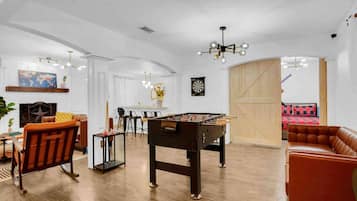A spacious living room with a foosball table, leather sofas, a dining area, and a dartboard.