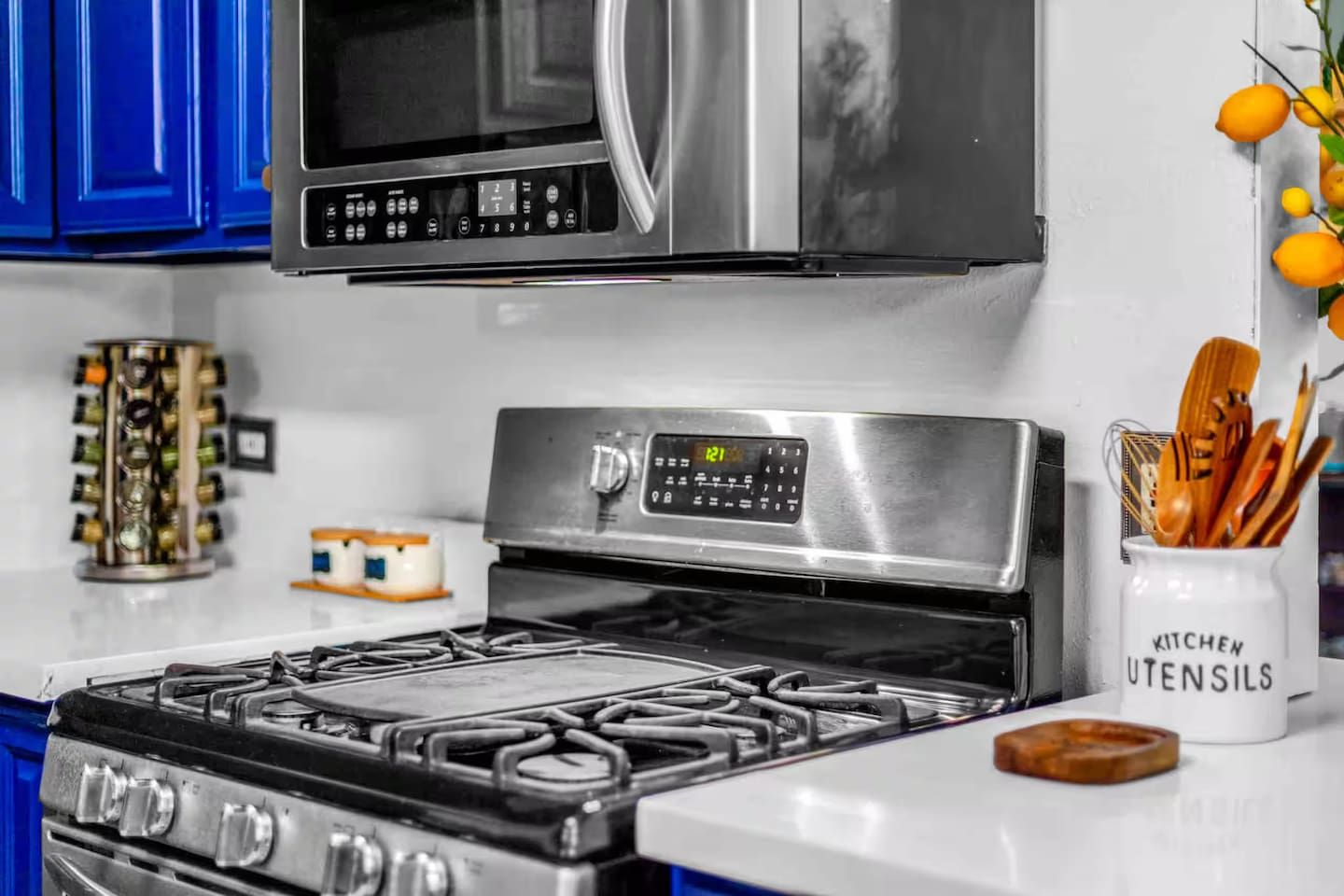 A kitchen with a stove, microwave, and a white cabinet labeled 'KITCHEN UTENSILS'.