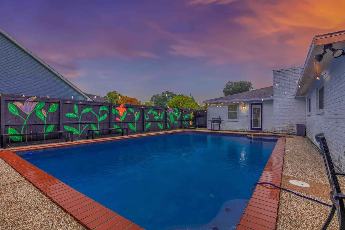 A swimming pool with a wooden deck and a fence with colorful graffiti.