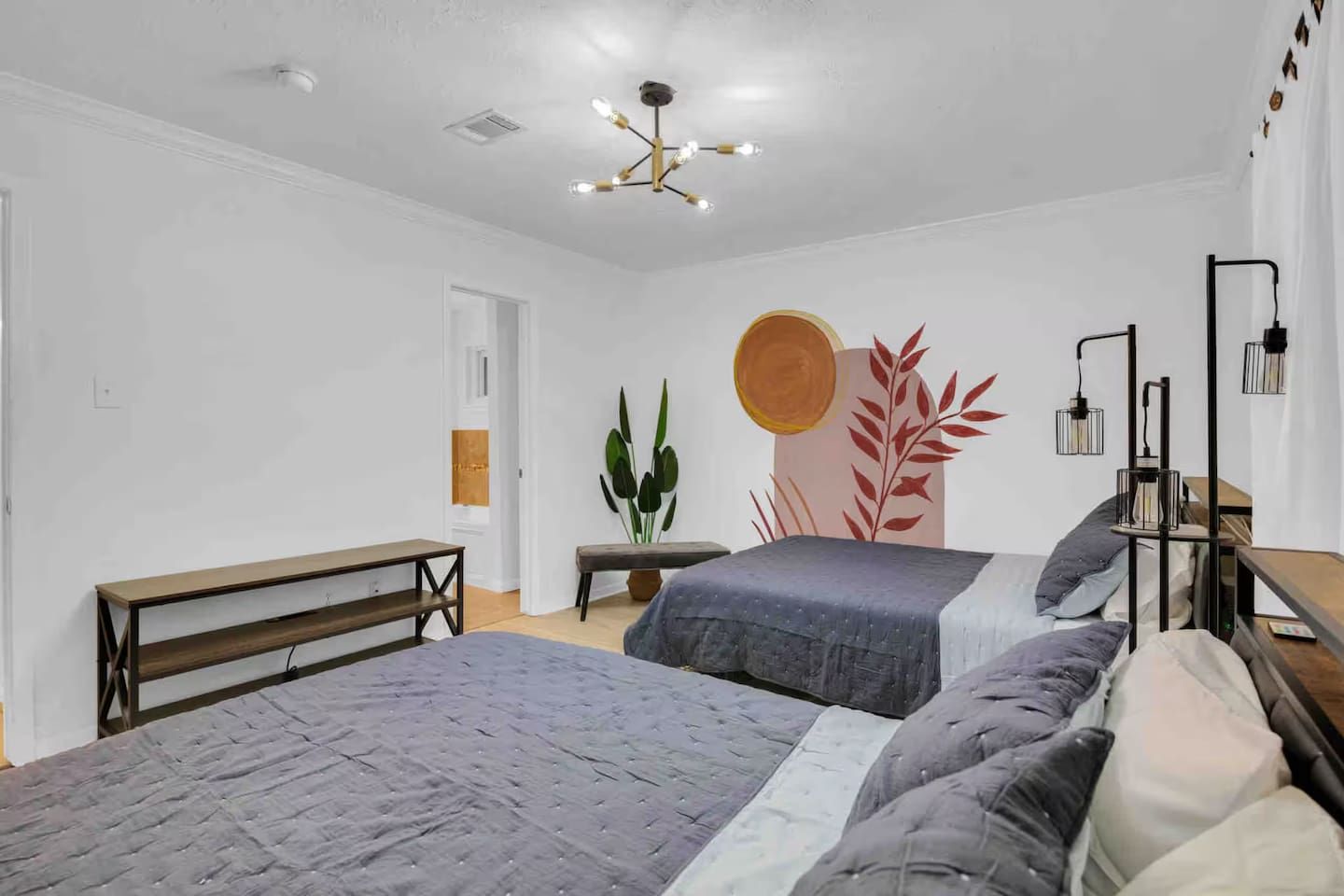 A bedroom with two beds, a bench, a plant, and a wall art piece.