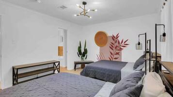 Une chambre avec deux lits, un banc, une plante et une œuvre d’art murale.