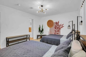 Un dormitorio con dos camas, un banco, una planta y una obra de arte en la pared.