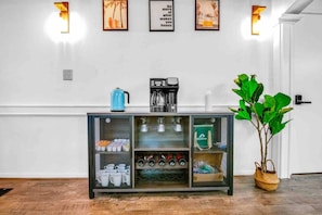 Un área de kitchenette con cafetera, hervidor y un armario con estantes de almacenamiento.
