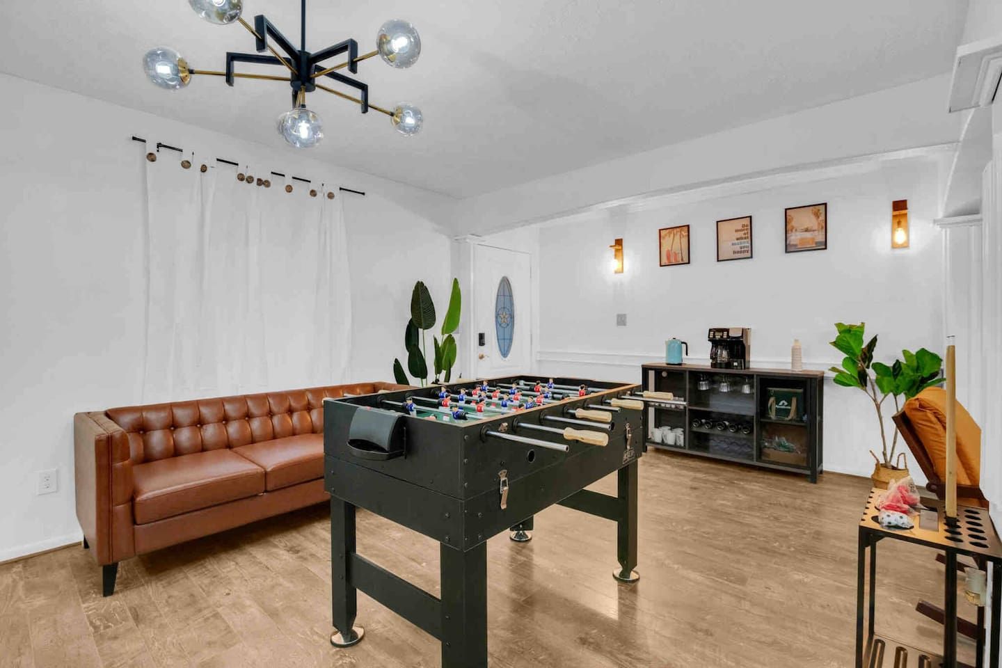 A room with a foosball table, a brown leather sofa, a coffee machine, and a plant.