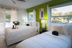 A hotel room with two beds, a window with a view, a bedside table with a lamp, and a vase with flowers. - TPA Fun Compound by Airport / Restaurants (Tampa)