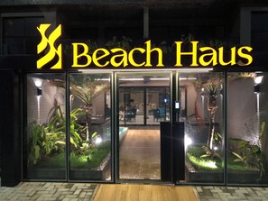 A hotel entrance with a glass facade, palm plants, and a sign reading 'Beach Haus'. - New Listing (João Pessoa)