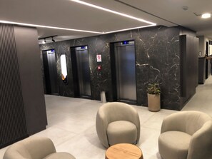 A modern lobby with marble walls, three elevators, and comfortable seating areas. - New Listing (João Pessoa)