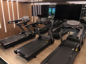 A gym with multiple treadmills arranged in rows, a large mirror, and a television mounted on the wall. - New Listing (João Pessoa)