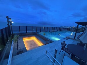 A rooftop pool area with a view of the ocean, a hot tub, and outdoor seating. - New Listing (João Pessoa)