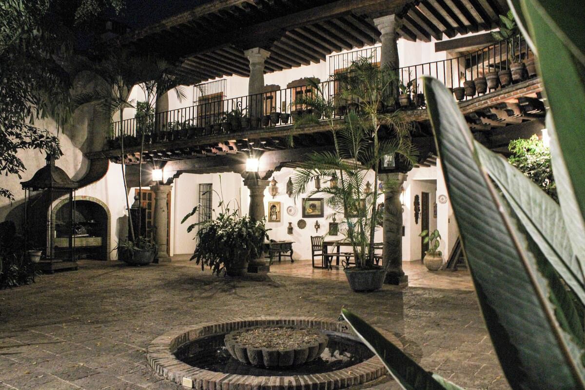 Un patio con un elemento acuático circular, plantas en macetas y un balcón con barandillas.