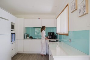 A modern kitchen with white cabinets, a teal backsplash, and a coffee machine. - Paradise Lake Conjola Park - Wake up to ocean views (Conjola Park)