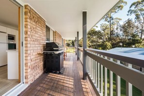 Un espacio al aire libre techado con una parrilla, una terraza de madera y vista a árboles.