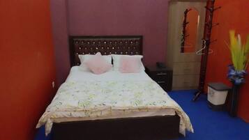 A bed with a floral bedspread and two pillows, a wooden headboard, a nightstand, a coat rack, and a small trash bin.