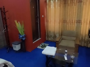 Una habitación con alfombra azul, un sofá, una mesa de vidrio con una botella y un pequeño cubo de basura.