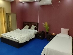 Una camera d'albergo con un letto grande, un letto più piccolo, un comodino e un condizionatore d'aria.
