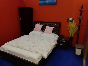 Una cama con cabecera, dos mesitas de noche, una mesita auxiliar, un perchero de pared y un cubo de basura.