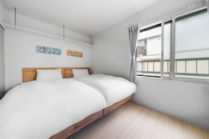A bedroom with a bed, two wall-mounted artworks, a window with curtains, and a wooden floor. - Billboard 110 (Sapporo)