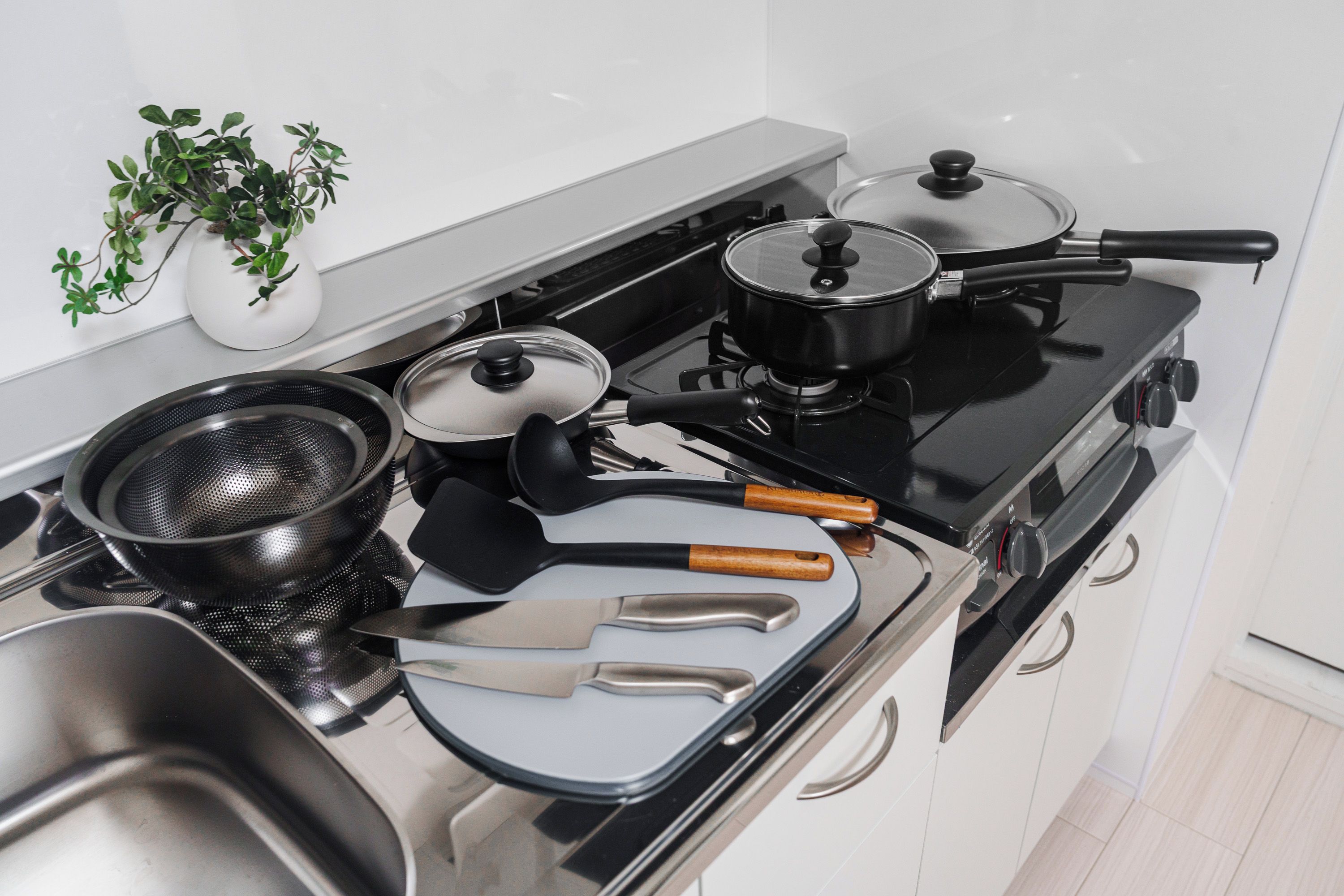 A kitchen with a stove, pots, pans, a strainer, and a knife.