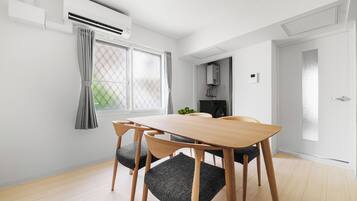 A modern dining area with a wooden table and chairs, an air conditioning unit, and a view of a kitchen area.
