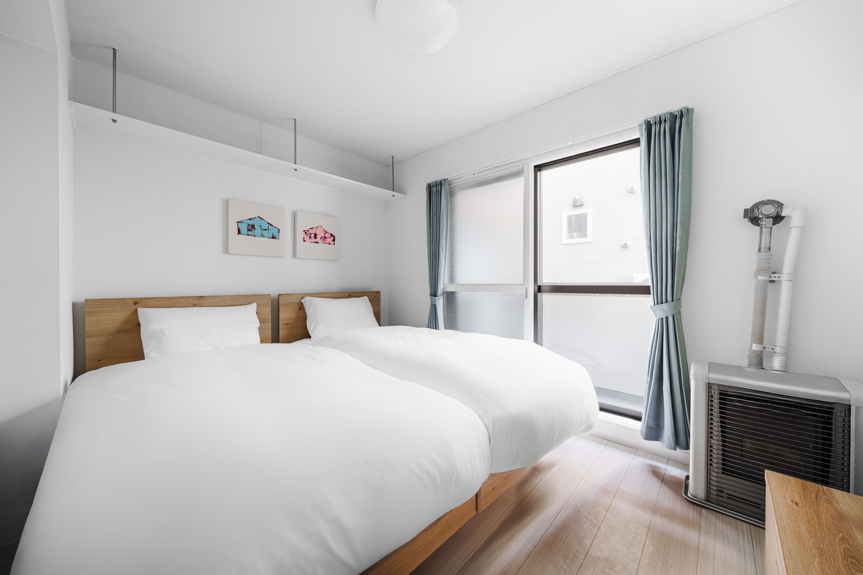 A hotel room with two beds, a window with curtains, a radiator, and artwork on the wall.