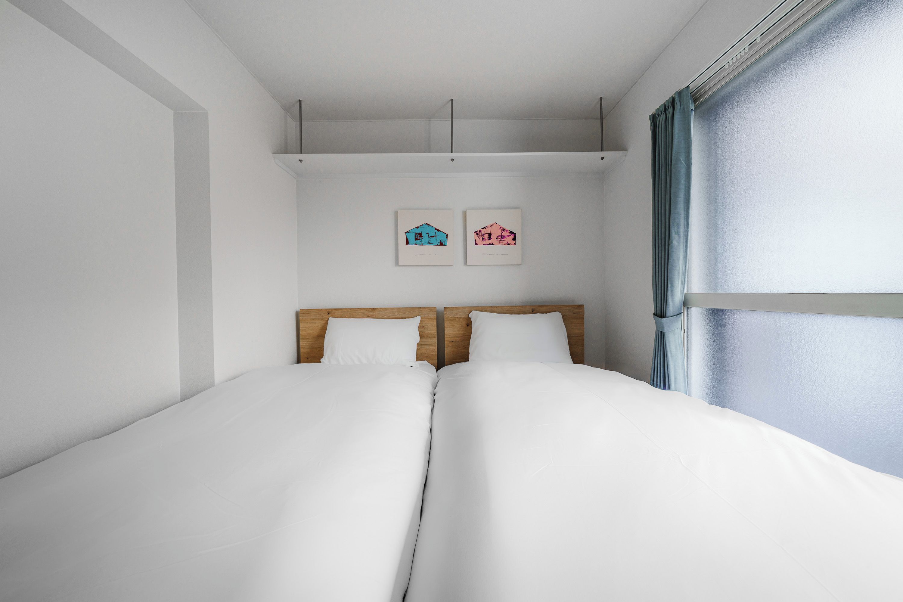 Een tweepersoonsbed met wit beddengoed, een houten hoofdbord en twee ingelijste foto's aan de muur.