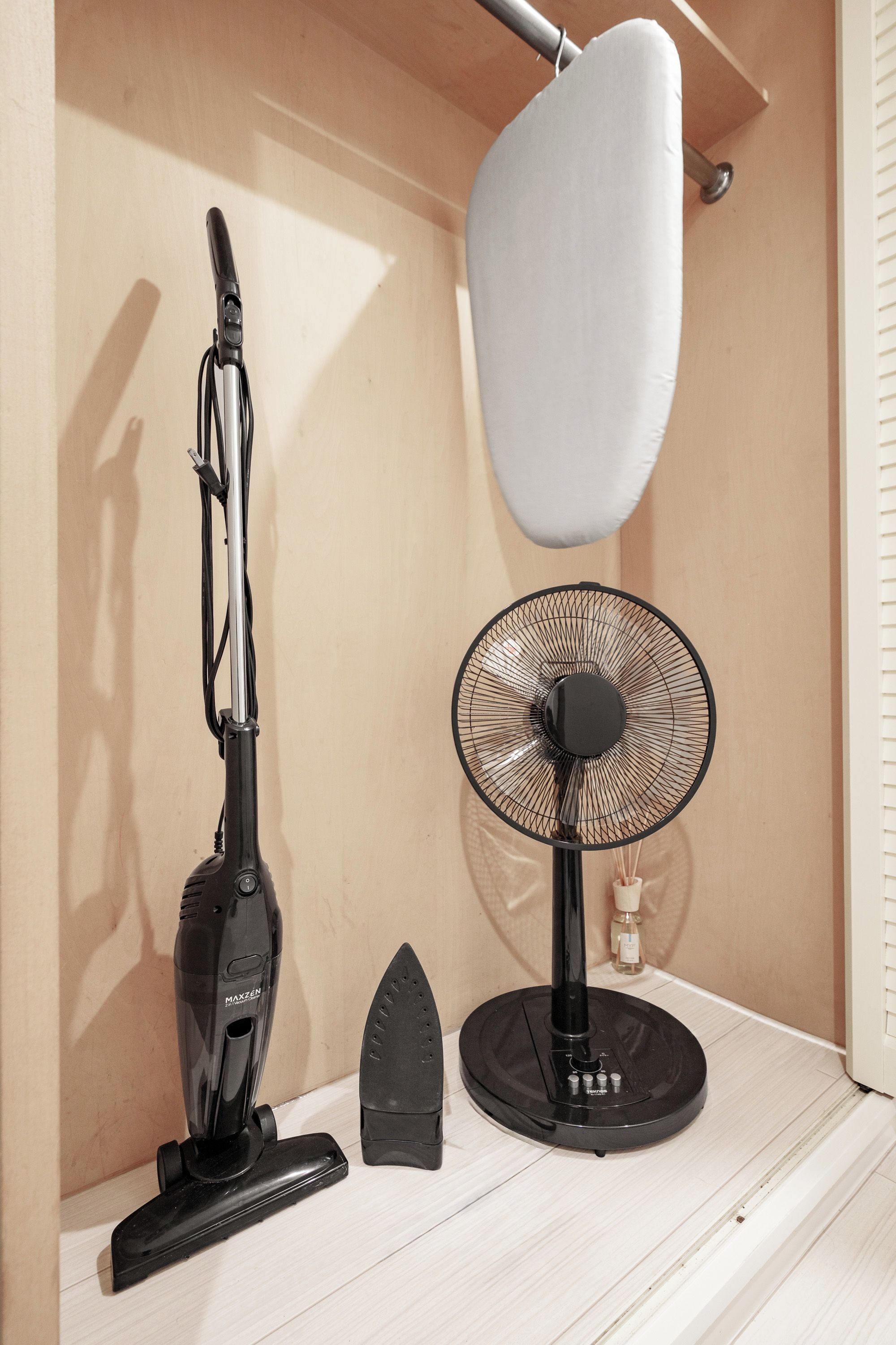 Een stofzuiger, een strijkijzer en een ventilator op een houten plank.