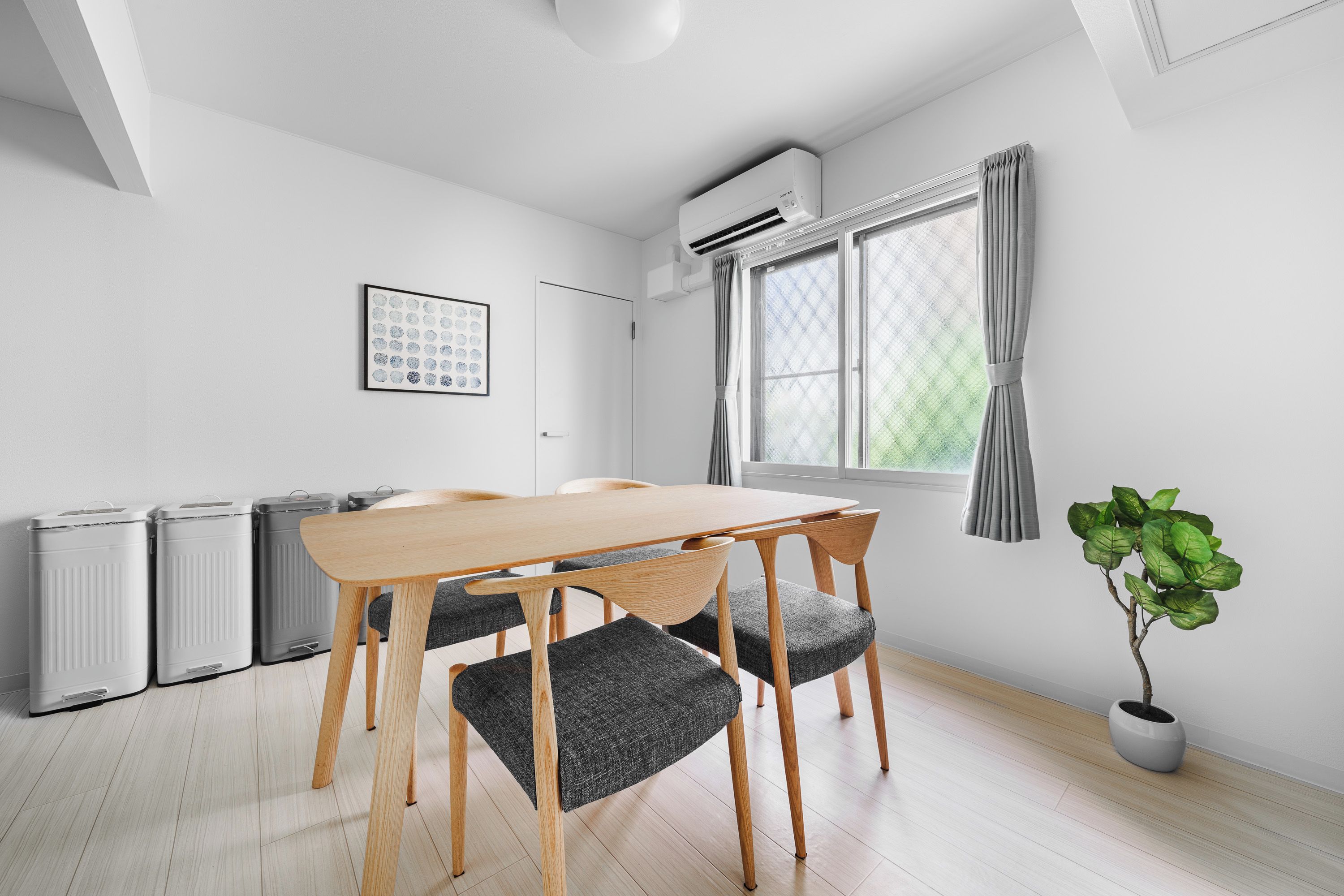 Een moderne, minimalistische kamer met een houten tafel en stoelen, een radiator, een raam met gordijnen en een potplant.