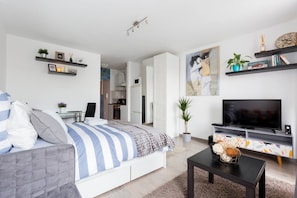 A modern bedroom with a bed, a TV, a desk, and a kitchenette. - Cozy Budapest Apartment Escape (Budapest)