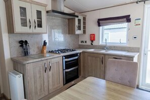 Une cuisine avec des meubles de rangement en bois, une cuisinière à gaz, un four et une fenêtre avec des rideaux.