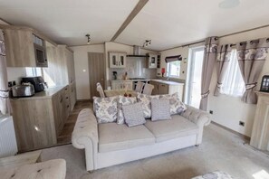 A compact living space with a kitchenette, a sofa with patterned cushions, and a window with curtains. - Lodge Sleeps 8 - Hot Tub - Dog Welcome (Lincoln)